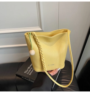 Detail of lemon yellow lychee texture bucket bag with woven strap and wood bead charm