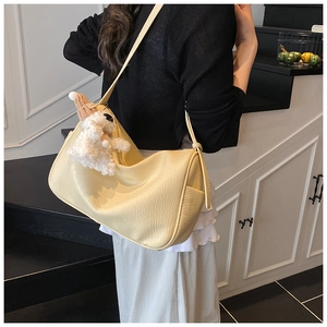 Detail view of a yellow leather shoulder bag with plush lamb charm and side pockets