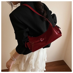 Detail of a deep red glossy leather underarm bag featuring decorative side flap pockets