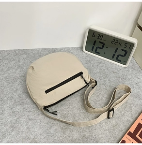 Détail d'un sac demi-lune en nylon beige avec bandoulière et poche à fermeture noire