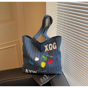 Close-up of blue and white striped denim tote bag with XQG lettering and paint splatters