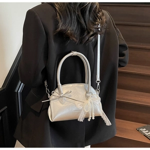 Borsa a conchiglia argento con fiocco indossata, finitura metallica e ciondolo di perle