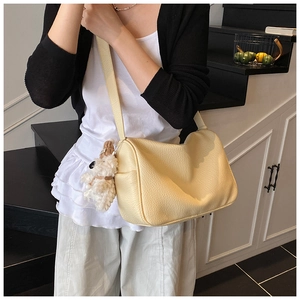 Nahaufnahme cremefarbene Schultertasche mit Litschi-Struktur und weißem Plüsch-Hundeanhänger