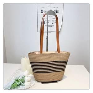 Detail view of woven straw tote bag featuring black stripes and brown leather straps