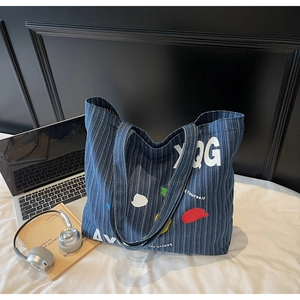 Detailed shot of large striped denim tote bag with colorful patches and laptop on bed
