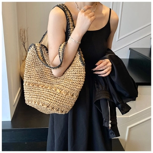 Detail of hand-woven straw tote bag with black strap worn by a model in a minimal setting