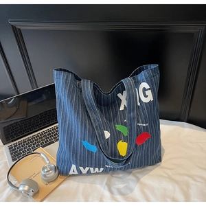 Detail view of large denim tote bag with colorful artistic prints and striped fabric texture