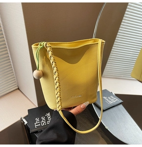 Detail view of yellow lychee leather bucket bag with woven strap and drawstring ornament