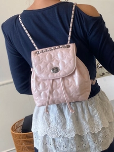 Pink star-quilted mini backpack with silver chain strap worn by a model in back view
