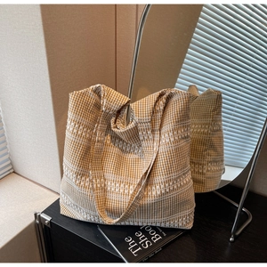 Detail of a brown gingham canvas tote bag with white embroidery and wide shoulder strap