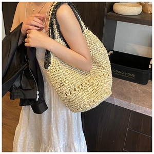 Detail of hand-woven straw tote bag with black braided handles in a home setting
