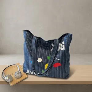 Detail of blue striped denim tote bag with colorful graphic prints and wide shoulder strap