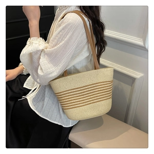 Detail of hand-woven straw tote with brown leather straps and striped patterns on model