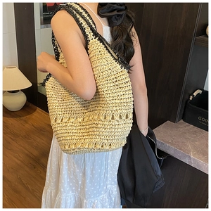 Detail of handwoven straw tote bag featuring contrast black shoulder straps and intricate patterns