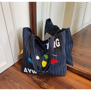 Detail of blue striped denim tote bag with colorful leaf pattern and large letters