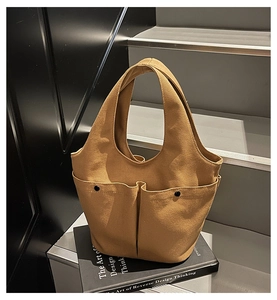Detail of khaki canvas tote bag featuring dual front pockets with black metal buckles