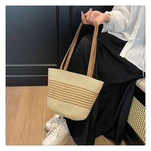 Detail of straw tote bag with brown leather handles held by a model in a resort setting