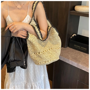 Close-up of a woven straw shoulder bag with black trim detailing worn by a model