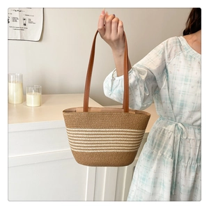 Detail of straw woven tote bag with white stripes and brown faux leather handle straps