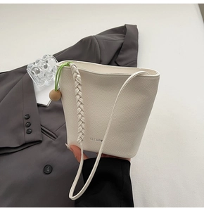 Detail of white litchi leather bucket bag with woven handle and green drawstring closure