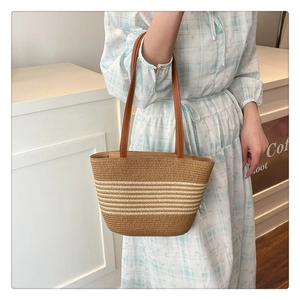 Close-up of straw woven tote bag with white stripes and brown leather strap on model