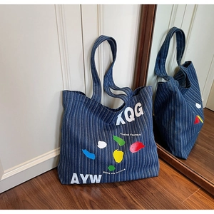 Detail of blue striped denim tote bag featuring colorful graffiti and finding yourself text