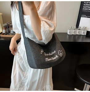 Détail du sac croissant en toile gris foncé avec broderie blanche et large bandoulière