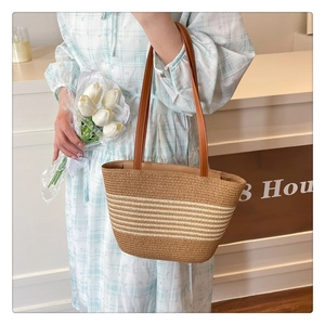 Close-up of natural straw tote bag with white stripes and brown leather handles