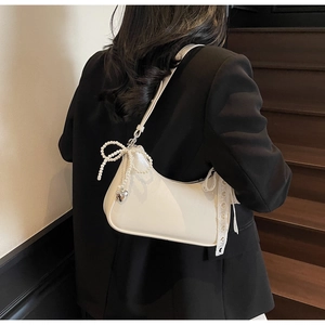 Dettaglio borsa sottobraccio in pelle bianco crema con fiocco di perle e ciondolo a cuore