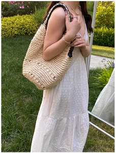 Outdoor lifestyle shot of a woven straw shoulder bag with black contrast trim on a model