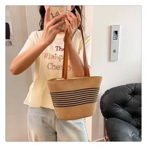 Detail view of woven straw tote bag with black stripes and brown leather handles