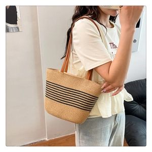 Detail view of woven straw tote bag with black stripes and brown leather straps