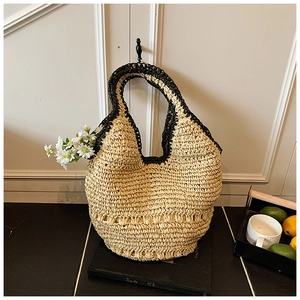 Detail of handwoven straw tote bag with black trim and hollow knit texture in summer setting