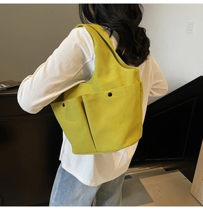 Detailed view of yellow-green canvas tote featuring large front pockets with black snap buttons