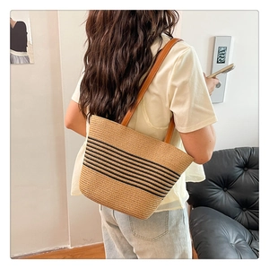 Detail of straw woven tote bag with black stripes and brown leather shoulder straps