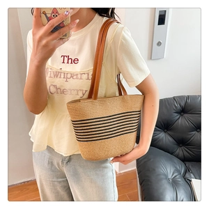 Detail of straw woven bucket bag with black stripes and brown leather shoulder strap
