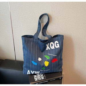 Detail view of blue striped denim tote bag with colorful paint splatter and XQG text print