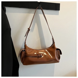 Detail of a brown patent leather underarm bag featuring side pockets and a glossy finish