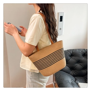 Detail of hand-woven straw tote with black stripes and brown leather handles on shoulder