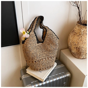 Detail of woven straw hobo bag with black trim and pink floral accent on a silver suitcase