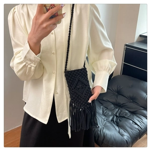 Détail d'un sac paille noir tissé main avec des pompons et des motifs géométriques