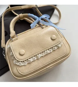 Detail view of beige crossbody bag with lace edges and checkered ribbon bow accessory