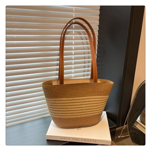 Detail of woven straw tote bag featuring brown leather handles with contrast stitching