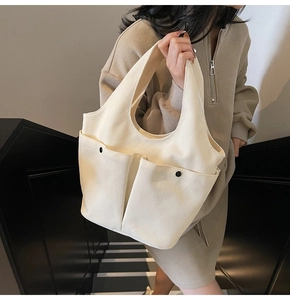 Detail view of cream canvas tote bag featuring double front pockets and black decorative buckles