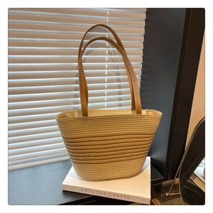 Detail of gradient straw woven tote bag with brown leather straps on a white book