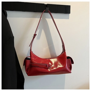 Detail view of red glossy patent leather underarm bag with decorative side pocket flap