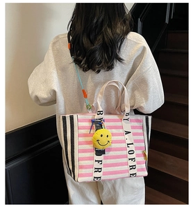 Detail of pink striped canvas tote bag with beige handles and yellow smiley charm