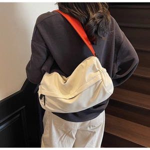 Detail view of large cream crossbody bag with ruched texture and orange shoulder strap