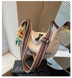 Detail of off-white dumpling bag with colorful striped strap and cartoon pendant