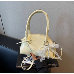 Dettaglio borsa a conchiglia crema con fiocco e ciondolo di perle su libro di moda